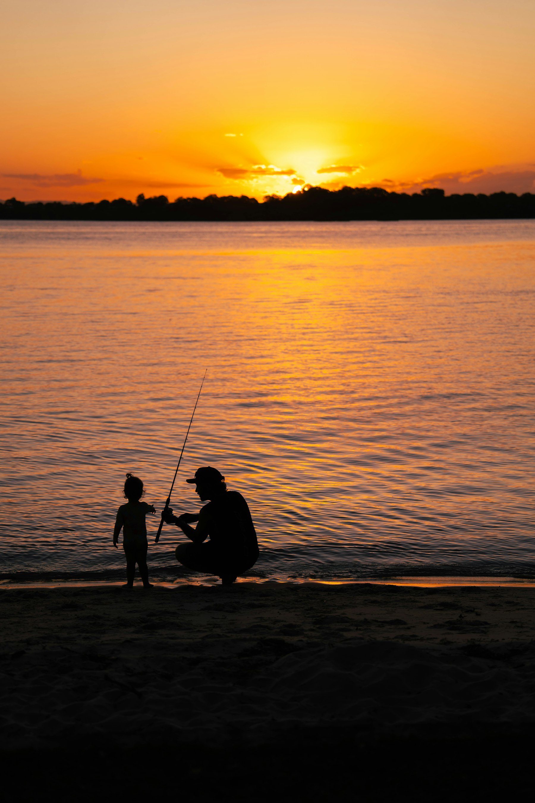Father teaching a toddler to hold a fishing rod against the sunset