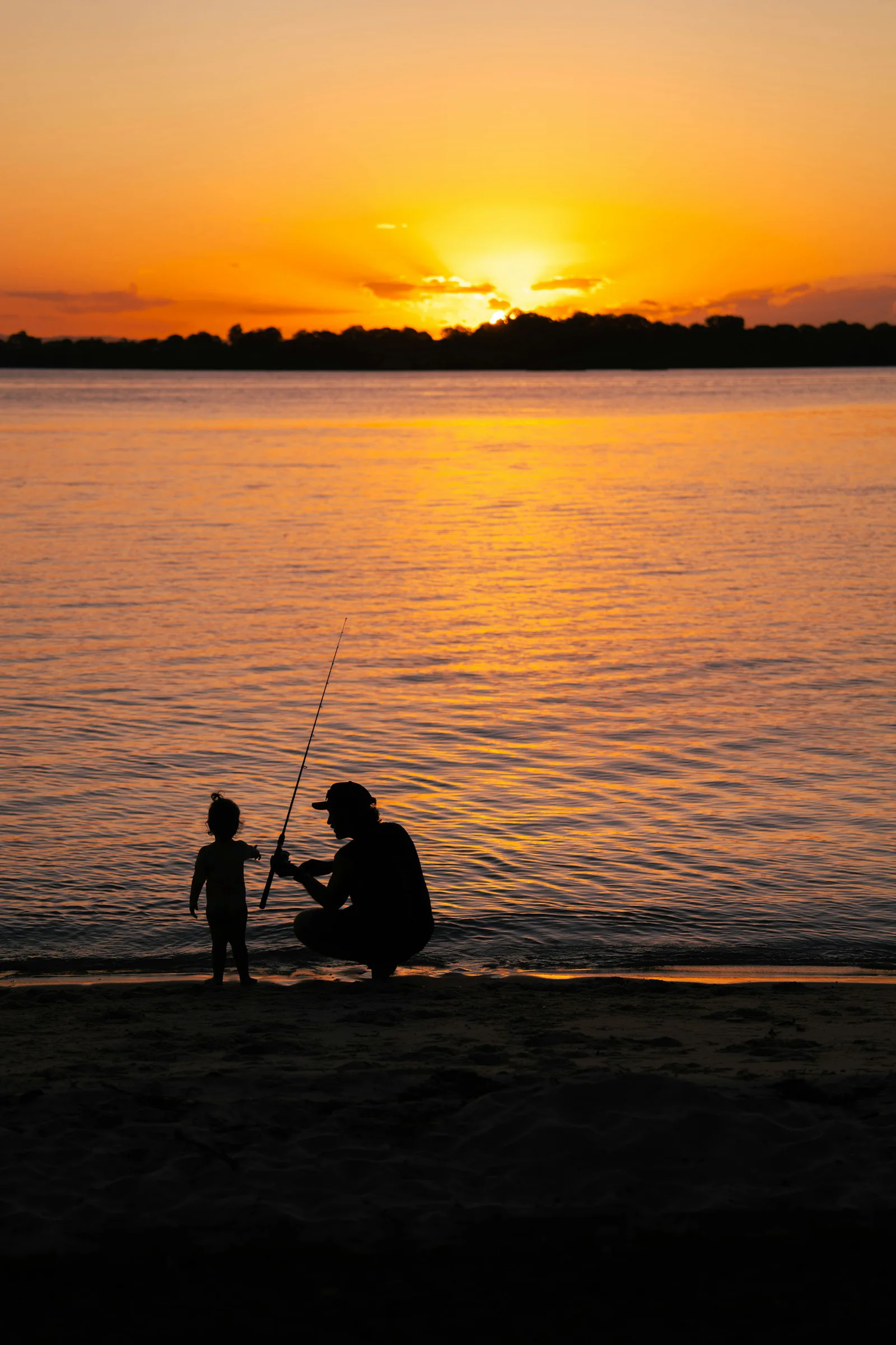 Representative photo of a parent teaching a young child to hold a fishing rod at sunset